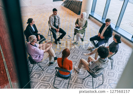 Top view of a diverse group of young business entrepreneurs gathered in a circle for a meeting, discussing corporate challenges and innovative solutions within the modern confines of a large 127568157