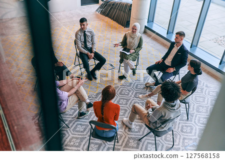 Top view of a diverse group of young business entrepreneurs gathered in a circle for a meeting, discussing corporate challenges and innovative solutions within the modern confines of a large 127568158