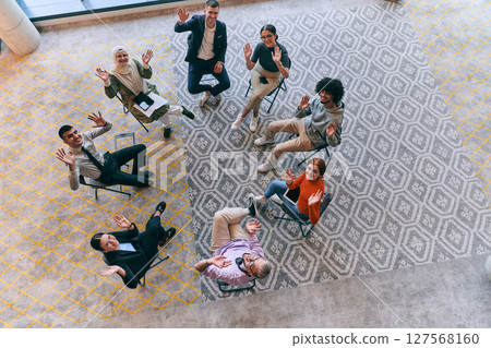 Top view of a diverse group of young business entrepreneurs gathered in a circle for a meeting, discussing corporate challenges and innovative solutions within the modern confines of a large 127568160