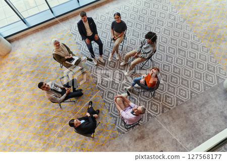 Top view of a diverse group of young business entrepreneurs gathered in a circle for a meeting, discussing corporate challenges and innovative solutions within the modern confines of a large 127568177