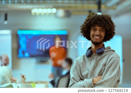In a modern office environment, an African American young entrepreneur with headphones engages in work, while in the background, his dedicated colleagues exemplify teamwork and collaboration 127568219