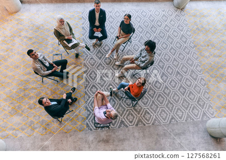 Top view of a diverse group of young business entrepreneurs gathered in a circle for a meeting, discussing corporate challenges and innovative solutions within the modern confines of a large 127568261