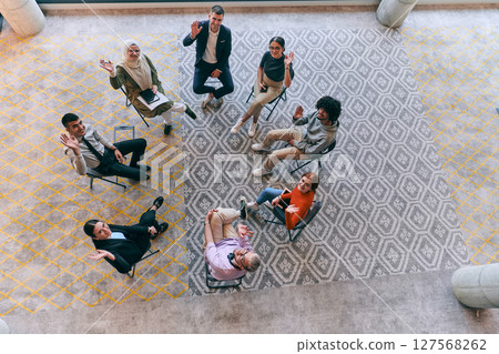 Top view of a diverse group of young business entrepreneurs gathered in a circle for a meeting, discussing corporate challenges and innovative solutions within the modern confines of a large 127568262