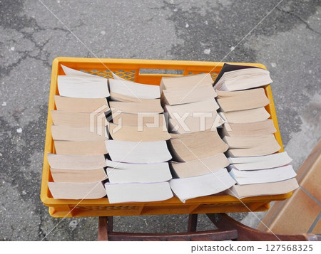 A crate full of books is sitting on a sidewalk 127568325