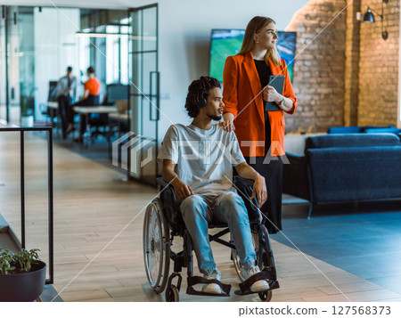 African-American businessman in a wheelchair engages in a collaborative discussion, using a tablet, with his business colleague, exemplifying the seamless integration of adaptive technology and African-American businessman in a wheelchair engages in a collaborative discussion, using a tablet, with his business colleague, exemplifying the seamless integration of adaptive technology and 127568373