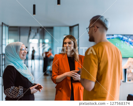 A group of young business colleagues, including a woman in a hijab, stands united in the modern corridor of a spacious startup coworking center, representing diversity and collaborative spirit A group of young business colleagues, including a woman in a hijab, stands united in the modern corridor of a spacious startup coworking center, representing diversity and collaborative spirit 127568374