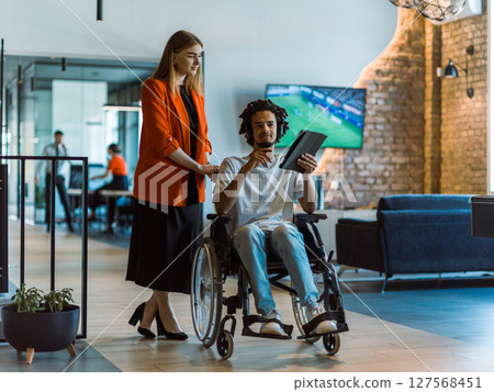 African-American businessman in a wheelchair engages in a collaborative discussion, using a tablet, with his business colleague, exemplifying the seamless integration of adaptive technology and African-American businessman in a wheelchair engages in a collaborative discussion, using a tablet, with his business colleague, exemplifying the seamless integration of adaptive technology and 127568451