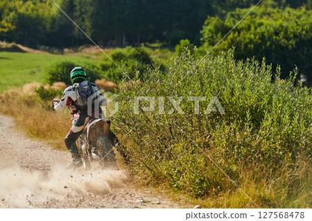 A professional motocross rider exhilaratingly riding a treacherous off-road forest trail on their motorcycle. 127568478