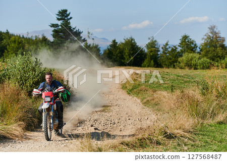 A professional motocross rider exhilaratingly riding a treacherous off-road forest trail on their motorcycle. 127568487