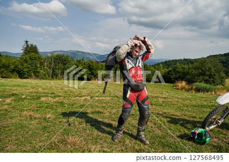 A professional motocross rider, clad in a full suit, gloves, and backpack, prepares for a daring adventure through the forest, geared up for an adrenaline-pumping off-road journey A professional motocross rider, clad in a full suit, gloves, and backpack, prepares for a daring adventure through the forest, geared up for an adrenaline-pumping off-road journey 127568495