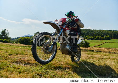 A fearless professional motocross rider skillfully executes an extreme back wheelie maneuver through a perilous forest terrain, showcasing remarkable balance and daring expertise A fearless professional motocross rider skillfully executes an extreme back wheelie maneuver through a perilous forest terrain, showcasing remarkable balance and daring expertise 127568498