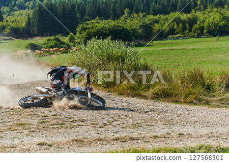 A professional motocross rider experiences an unfortunate fall from their motorcycle on a forest trail, highlighting the dangers of off-road racing. 127568501