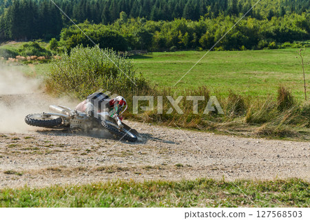 A professional motocross rider experiences an unfortunate fall from their motorcycle on a forest trail, highlighting the dangers of off-road racing. 127568503