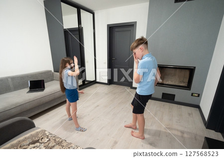Two children engaging in a playful dance competition in a modern living room filled with natural light during the afternoon 127568523