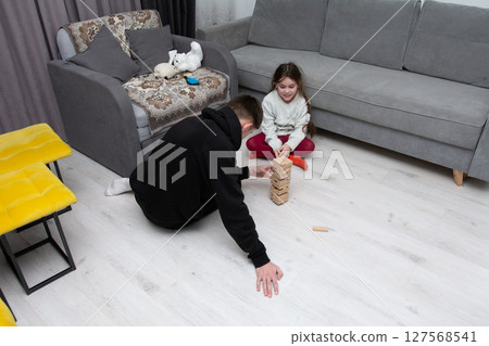 Playful moments in a cozy living room as a child and adult build a tower with wooden blocks, capturing the joy of family time on a winter evening Playful moments in a cozy living room as a child and adult build a tower with wooden blocks, capturing the joy of family time on a winter evening 127568541