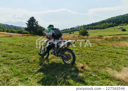 A motorcyclist equipped with professional gear, rides motocross on perilous meadows, training for an upcoming competition. A motorcyclist equipped with professional gear, rides motocross on perilous meadows, training for an upcoming competition. 127568546