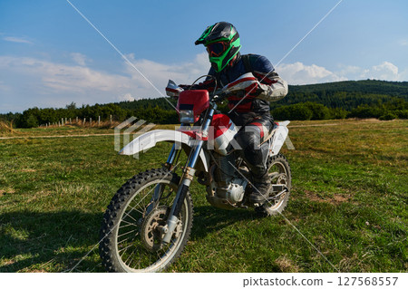 A motorcyclist equipped with professional gear, rides motocross on perilous meadows, training for an upcoming competition. 127568557