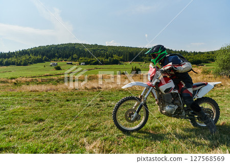 A motorcyclist equipped with professional gear, rides motocross on perilous meadows, training for an upcoming competition. 127568569