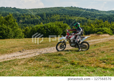 A motorcyclist equipped with professional gear, rides motocross on perilous meadows, training for an upcoming competition. 127568570