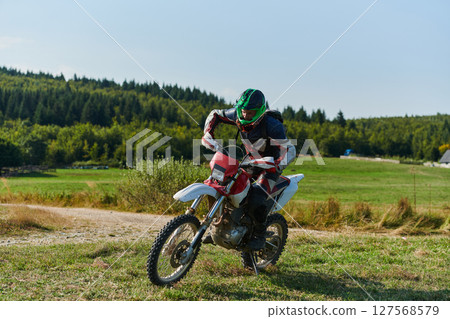 A professional motocross rider starting their motorcycle, poised to begin a high-adrenaline training session on a hazardous forest trail, embodying the spirit of off-road adventure A professional motocross rider starting their motorcycle, poised to begin a high-adrenaline training session on a hazardous forest trail, embodying the spirit of off-road adventure 127568579