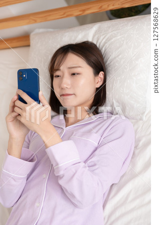 A young woman operating a smartphone while lying in bed 127568629