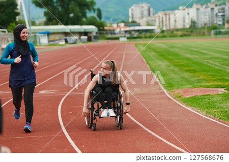 A Muslim woman in a burqa running together with a woman in a wheelchair on the marathon course, preparing for future competitions. 127568676