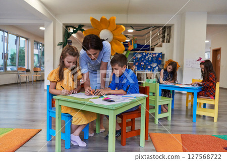 Creative kids during an art class in a daycare center or elementary school classroom drawing with female teacher. 127568722