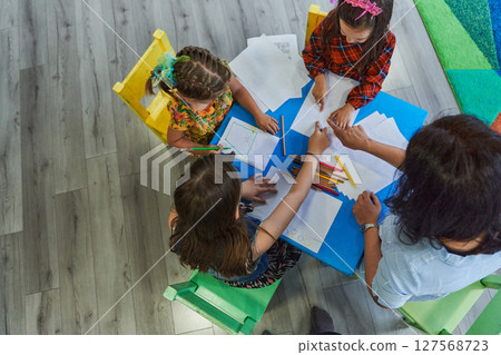 Creative kids during an art class in a daycare center or elementary school classroom drawing with female teacher. 127568723