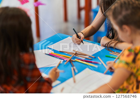 Close up photo of kids during an art class in a daycare center or elementary school classroom drawing with female teacher. 127568746