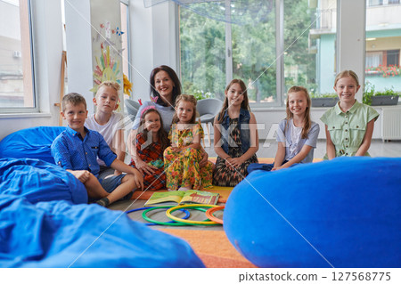 A happy female teacher sitting and playing hand games with a group of little schoolchildren 127568775