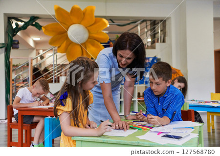 Creative kids during an art class in a daycare center or elementary school classroom drawing with female teacher. Creative kids during an art class in a daycare center or elementary school classroom drawing with female teacher. 127568780