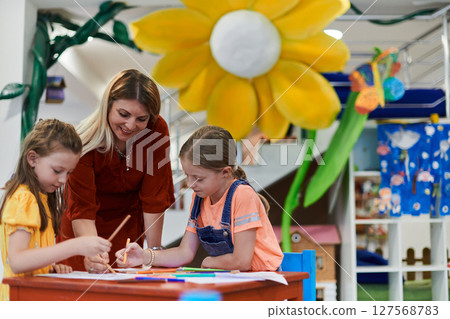 Creative kids during an art class in a daycare center or elementary school classroom drawing with female teacher. 127568783