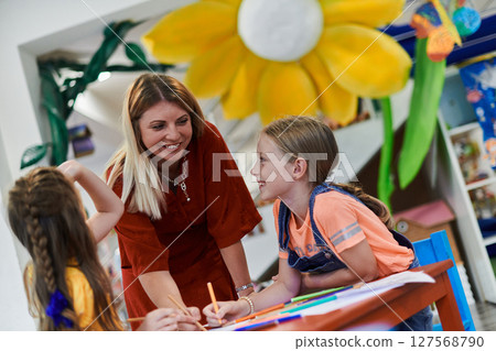 Creative kids during an art class in a daycare center or elementary school classroom drawing with female teacher. 127568790