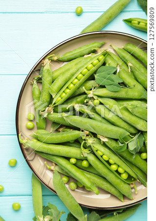 Fresh green peas in wooden bowl with pods and leaves on blue wooden background, healthy green vegetable or legume Fresh green peas in wooden bowl with pods and leaves on blue wooden background, healthy green vegetable or legume 127569809