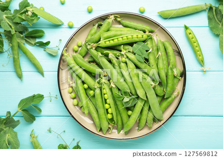 Fresh green peas in wooden bowl with pods and leaves on blue wooden background, healthy green vegetable or legume Fresh green peas in wooden bowl with pods and leaves on blue wooden background, healthy green vegetable or legume 127569812
