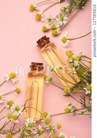 Bottles of essential oil and chamomile flowers on pink background. Vertical photo 127569818