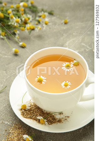 Aromatic herbal tea in white cup and chamomiles on grey concrete background. Vertical photo Aromatic herbal tea in white cup and chamomiles on grey concrete background. Vertical photo 127569832