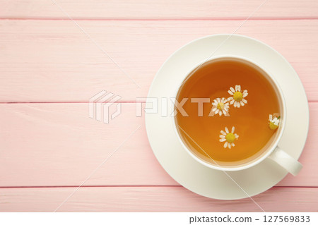 Aromatic herbal tea in white cup and chamomiles on pink background. Space for text 127569833