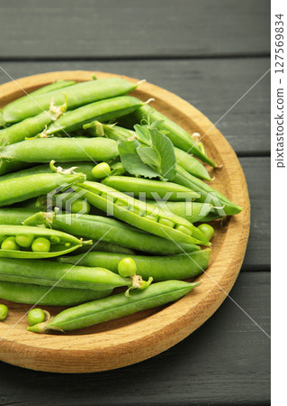 Fresh green peas in wooden bowl with pods and leaves on black wooden background. Vertical photo 127569834