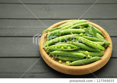 Fresh green peas in wooden bowl with pods and leaves on black wooden background, healthy green vegetable or legume 127569835