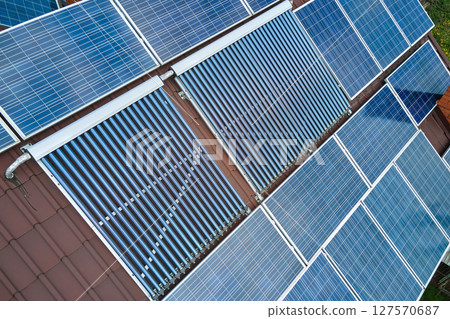 Building roof with rows of blue photovoltaic panels and vacuum air solar collectors for water heating and producing clean ecological electricity. Renewable electric and heat energy with zero emission 127570687