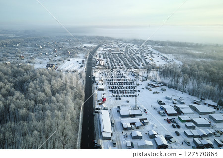 Aerial view of winter landscape with snow covered woods and black asphalt forest road on cold wintry day 127570863