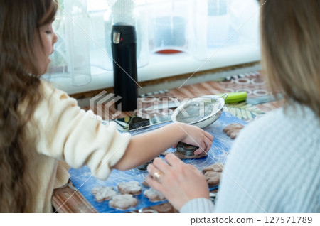 A child and adult bake together, using cookie cutters to shape dough. A fun family activity. 127571789