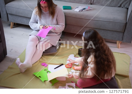 Mother and daughter crafting together, creating handmade cards and decorations. A cozy moment of shared creativity. Mother and daughter crafting together, creating handmade cards and decorations. A cozy moment of shared creativity. 127571791