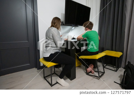On a cozy evening at home, a child is deeply engaged in a focused study session while a parent provides supportive guidance, creating a warm learning atmosphere On a cozy evening at home, a child is deeply engaged in a focused study session while a parent provides supportive guidance, creating a warm learning atmosphere 127571797
