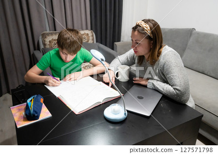 On a cozy evening at home, a child is deeply engaged in a focused study session while a parent provides supportive guidance, creating a warm learning atmosphere 127571798