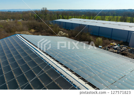 Aerial view of solar power plant with blue photovoltaic panels mounted on industrial building roof for producing green ecological electricity. Production of sustainable energy concept Aerial view of solar power plant with blue photovoltaic panels mounted on industrial building roof for producing green ecological electricity. Production of sustainable energy concept 127571823