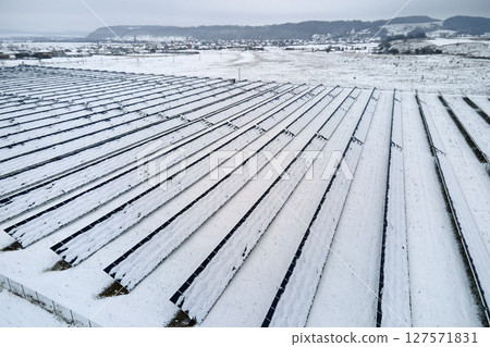 Aerial view of snow covered sustainable electric power plant with rows of solar photovoltaic panels for producing clean electrical energy. Low effectivity of renewable electricity in northern winter Aerial view of snow covered sustainable electric power plant with rows of solar photovoltaic panels for producing clean electrical energy. Low effectivity of renewable electricity in northern winter 127571831