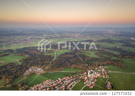 Aerial view of small town with red tiled roofs among green farm fields and distant forest in summer. Aerial view of small town with red tiled roofs among green farm fields and distant forest in summer. 127571832