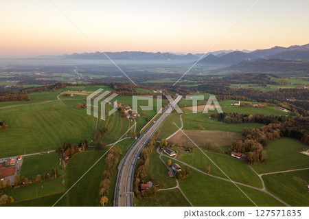 Aerial view of small scattered farm houses with red tiled roofs among green farming fields and distant mountain forest in summer. 127571835